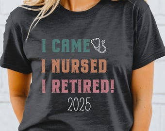 May include: A dark gray t-shirt with the text "I came, I nursed, I retired! 2025" in a vintage style font. The text is in shades of teal, orange, and pink. A small stethoscope icon is next to the word "came".