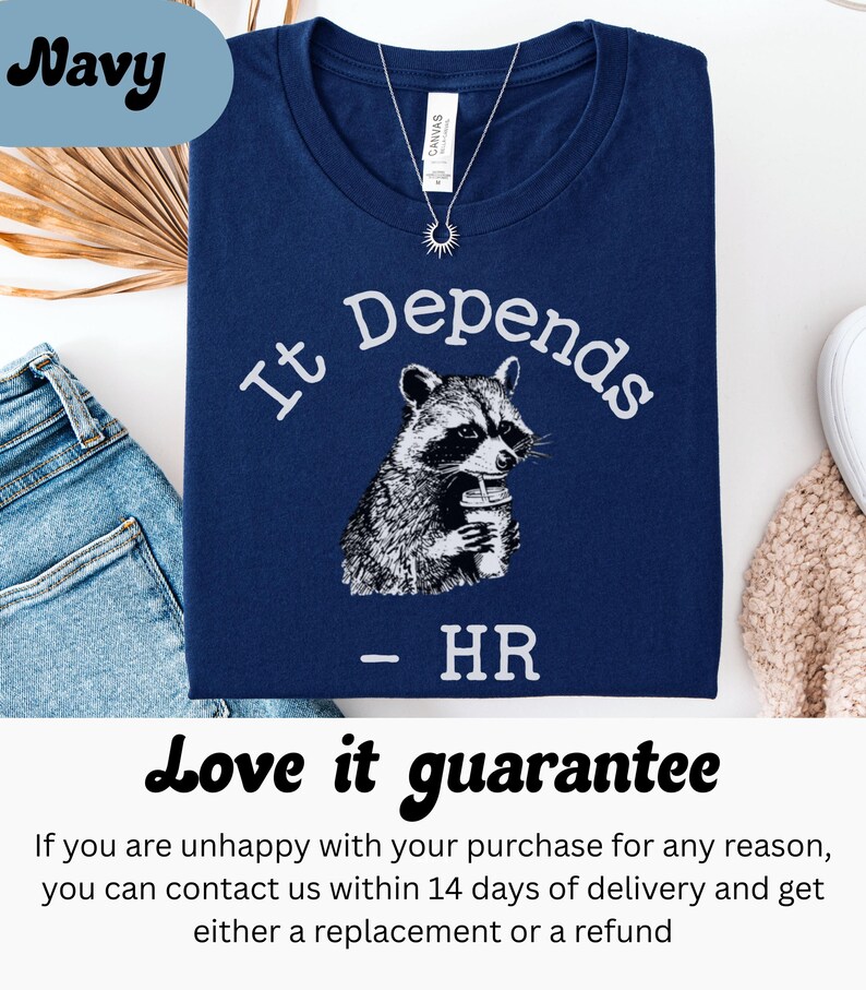 May include: Navy blue t-shirt with the text "It Depends" above a raccoon illustration holding a beverage. Below the raccoon is the text "- HR". A silver necklace with a sun pendant is visible.