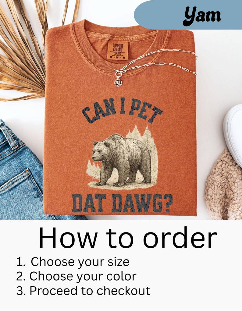May include: A burnt orange t-shirt with the text "CAN I PET DAT DAWG?" and a graphic of a bear. The shirt also has the Comfort Colors logo and a silver necklace. The image includes instructions on how to order.