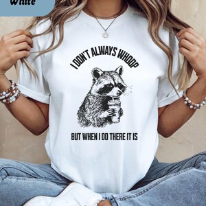 May include: White t-shirt with a raccoon graphic holding a drink. The text reads "I DON'T ALWAYS WHOOP BUT WHEN I DO THERE IT IS" in black. The shirt is a casual style.