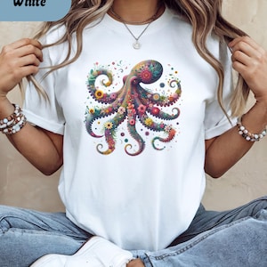May include: White t-shirt featuring a colorful floral octopus design. The octopus is adorned with various flowers in shades of pink, yellow, and purple. The word "White" is in a light blue box in the upper left corner.