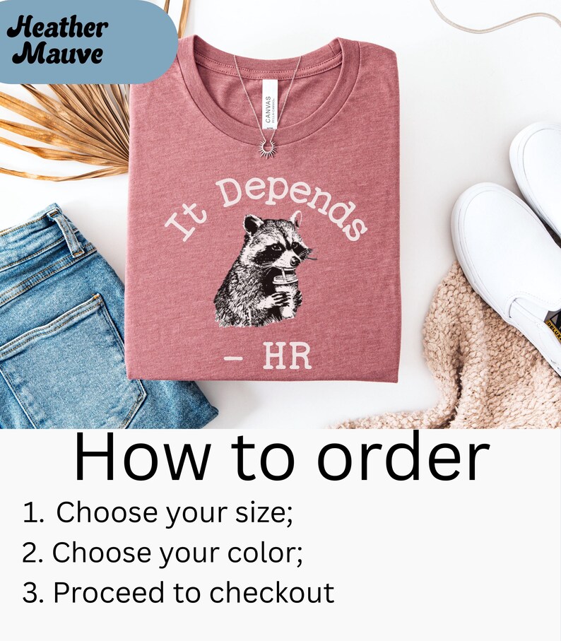 May include: Heather mauve t-shirt with the text "It Depends" and a raccoon graphic holding a cup. The shirt also has the text "- HR" below the raccoon. The shirt is folded and placed on a white surface with blue jeans and white shoes.