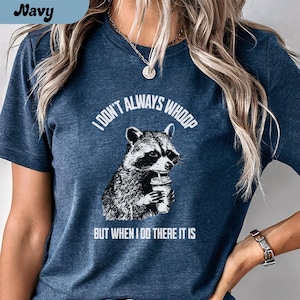 May include: Heather navy t-shirt with a raccoon graphic holding a cup. The text reads "I don't always whoop but when I do there it is." The shirt is a dark blue color.