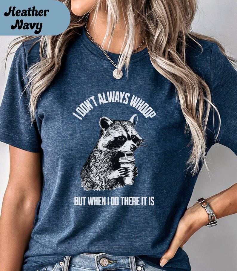May include: Heather navy t-shirt with a raccoon graphic holding a cup. The text reads "I don't always whoop but when I do there it is." The shirt is a dark blue color.
