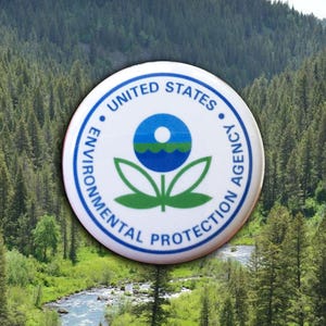 May include: A round white button with the text "UNITED STATES ENVIRONMENTAL PROTECTION AGENCY" encircling a blue and green logo. The background is a scenic view of a river and forest.