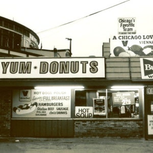 May include: A vintage sign for Yum-Yum Donuts with a red and white Budweiser sign above it. The sign is located in Wrigleyville, Chicago, and advertises a full breakfast menu, hot dogs, polish sausage, and cold drinks.