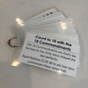 May include: A set of white rectangular cards held together by a silver metal ring. The top card features black text that reads: Count to 10 with the 10 Commandments. The 10 Commandments are God's law for how to live. Only Jesus obeyed the law perfectly.