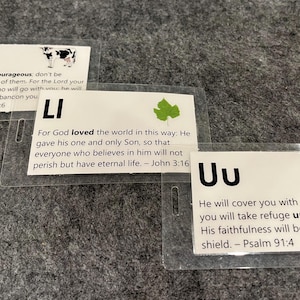 Może przedstawiać: Trzy kolorowe karty z nadrukowanymi literami "Cc", "Li" i "Uu". Każda karta ma inny obrazek i wydrukowany werset biblijny. Karta "Cc" ma krowę, karta "Li" ma zielony liść, a karta "Uu" ma niebieski parasol.