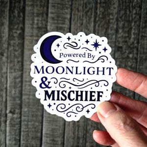 Enchanting "Powered by Moonlight & Mischief" vinyl sticker. This mystical sticker features a gorgeous crescent moon surrounded by twinkling stars and celestial flourishes in dreamy purple hues - perfect for night owls, lunar lovers, and witchy souls who do their best work when the sun goes down.