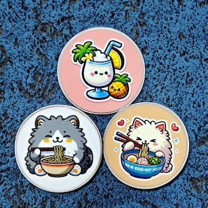 May include: Three round, white, ceramic coasters with colorful cartoon images. The first coaster features a gray cat eating ramen noodles. The second coaster features a white cat eating ramen noodles. The third coaster features a cartoon pineapple drink with a straw and a palm tree.