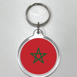 Puede incluir: Llavero acrílico transparente con la bandera de Marruecos. El llavero tiene un fondo rojo con una estrella verde en el centro. El llavero está unido a un llavero de metal plateado.