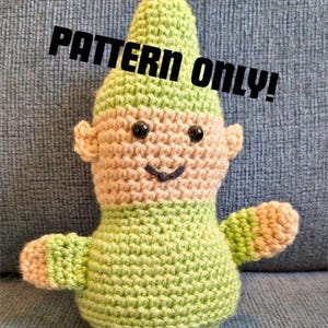 Può includere: Una bambola di gnomo all'uncinetto fatta a mano nei toni del verde e del beige. Lo gnomo ha un cappello a punta, piccole orecchie e un viso sorridente con occhi a bottone neri. Il testo "PATTERN ONLY!" è stampato sull'immagine.