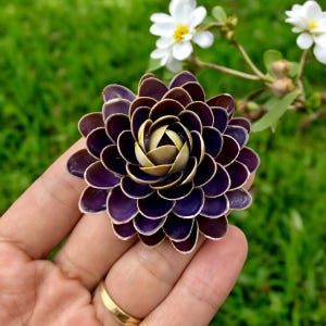Könnte beinhalten: Eine lila und goldene Blume aus Muscheln. Die Blume wird in einer Hand gehalten.