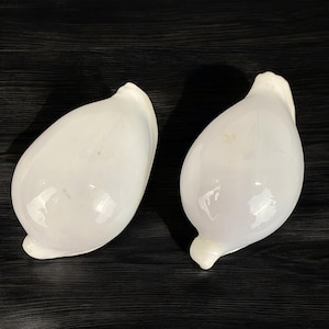 May include: Two white ceramic egg-shaped objects with a smooth, glossy finish. The objects are similar in shape and size, and they are both oriented with the pointed end facing the viewer.