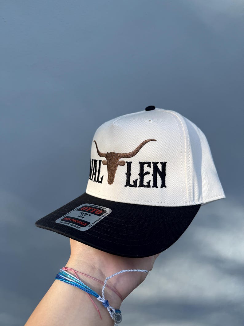 May include: White and black baseball cap with a brown bull's head and the text "VAL LEN" embroidered on the front.