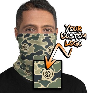 May include: A green, brown, and beige camouflage face mask with a white circle that says "Your Logo Here" in black text. The text "Your Custom Logo" is written in black and white above the mask.