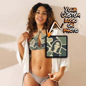 May include: A camouflage print bikini top with a halter neckline and a custom square graphic insert featuring a portrait. The text "YOUR CUSTOM LOGO OR PHOTO" is displayed in orange and black lettering with an arrow pointing to the graphic.