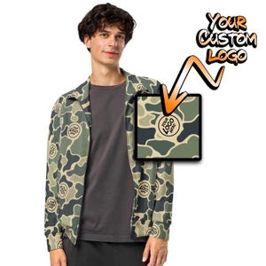 May include: A green and brown camouflage jacket with a zipper closure. The jacket has a pattern of small circles with the text "YOUR LOGO HERE" inside. The text "YOUR CUSTOM LOGO" is written in a graffiti style above the jacket.