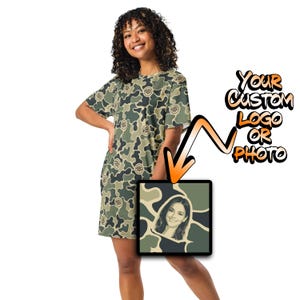 May include: A short-sleeve t-shirt dress featuring a green, brown, and black camouflage pattern. The dress includes a square graphic area displaying a portrait of a person, with text to the right reading Your Custom Logo Or Photo.