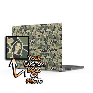 May include: A laptop skin featuring a green, tan, and black camouflage pattern with a repeating circular logo. A square inset displays a portrait of a person, and the text "YOUR CUSTOM LOGO OR PHOTO" appears in orange and black lettering below.