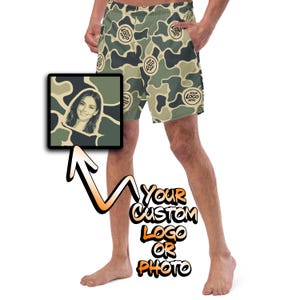 May include: Customizable swim trunks featuring a camouflage pattern in shades of olive green, tan, and dark gray. The shorts include repeating circular placeholders with the text "YOUR LOGO HERE" and a square inset showing a portrait photo.