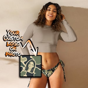 May include: A long-sleeved beige cropped top paired with camouflage print bikini bottoms featuring side ties. A square graphic overlay displays a portrait of a person against a camo background with the text "YOUR CUSTOM LOGO OR PHOTO".