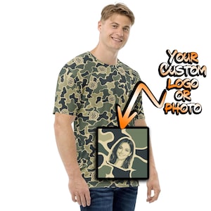 May include: A short-sleeve t-shirt featuring an all-over green, tan, and dark brown camouflage pattern with small circular logo placeholders. An orange arrow points to a square graphic displaying a portrait of a smiling person on a camo background.