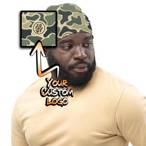 May include: A camouflage patterned beanie with a space for a custom logo. The logo is a circle with the text "YOUR LOGO HERE".