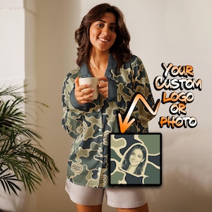 May include: A long-sleeved button-down pajama shirt featuring a green, gray, and black camouflage pattern. The shirt includes a white mug and a square graphic insert displaying a portrait of a person with the text Your Custom Logo Or Photo.