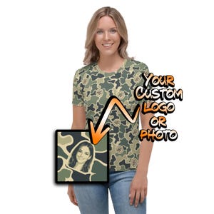 May include: A short-sleeved t-shirt featuring an all-over green, tan, and dark brown camouflage pattern with small circular logo icons. An orange arrow points to a square graphic showing a portrait of a person with the text YOUR CUSTOM LOGO OR PHOTO.