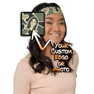 May include: A camouflage patterned headband featuring a customizable square graphic area. The design includes a placeholder for a logo or photo, with the text YOUR CUSTOM LOGO OR PHOTO displayed prominently in orange and white lettering.