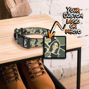 May include: A camouflage patterned pet collar with a black plastic buckle and a square graphic insert featuring a portrait of a person against a matching camo background, with text reading YOUR CUSTOM LOGO OR PHOTO and an orange arrow pointing down.