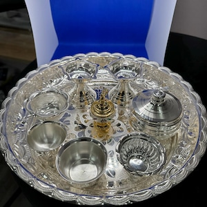 May include: A silver tray with a decorative design, containing a variety of silver bowls and dishes, including two small bowls with a gold accent, a small lidded container, and a small incense burner.