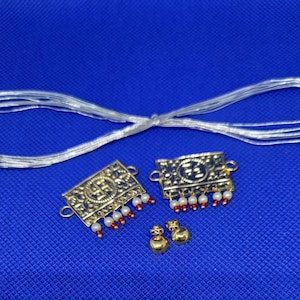 May include: A set of gold-colored jewelry with a white string. The jewelry includes two rectangular pendants with red and white beads and a small round pendant.