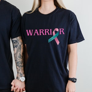 May include: Black t-shirt with the word "WARRIOR" in pink letters and a pink ribbon with the word "PREVIVOR" in teal letters.