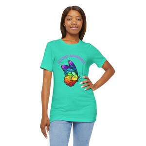 May include: A turquoise blue t-shirt with a rainbow butterfly graphic and the text "Ostomy Awareness" in purple.