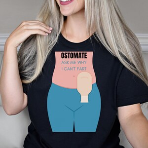 May include: Black t-shirt with a white graphic of a person wearing blue pants and an ostomy bag. The text on the graphic reads "Ostomate Ask Me Why I Can't Fart".