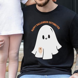 May include: Black t-shirt with a white ghost graphic and the text "HAPPY HALLOWEEN OSTOMATES" in orange. The ghost has a smiling face and a small brown patch. The shirt is worn by a person.