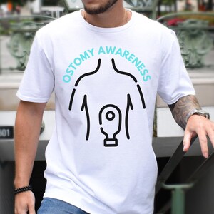 May include: White t-shirt with a black outline of a person with an ostomy bag and the text "Ostomy Awareness" in a blue circle.