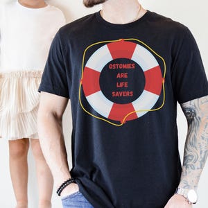May include: A black t-shirt with a red and white life preserver graphic. The life preserver has the text "Ostomies Are Life Savers" printed on it.