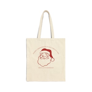 May include: Cream-colored tote bag with a red Santa Claus graphic and the text "MERRY CHRISTMAS TO ALL PREVIVORS" and "BRCA AWARENESS". The bag has two handles and is made of a canvas-like material.