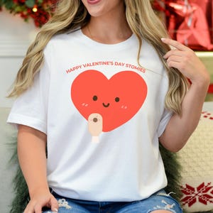 May include: White t-shirt with a red heart graphic and the text "Happy Valentine's Day Stomies".