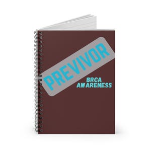 May include: A spiral-bound notebook with a dark brown cover. The notebook features the word "PREVIVOR" in light blue, overlaid on a gray rectangle. Below, the text "BRCA AWARENESS" is also in light blue.