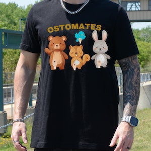 May include: Black t-shirt with the text "Ostomates" in gold lettering. The shirt features a cartoon bear, squirrel, and rabbit.