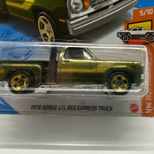 May include: A green 1978 Dodge Li'l Red Express Truck toy car with gold wheels and a gold stripe on the side. The car is in a plastic display case with a blue background and the text "1978 Dodge Li'l Red Express Truck" on the bottom.