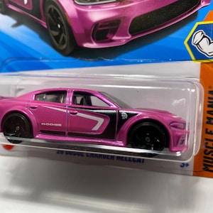 May include: A pink 20 Dodge Charger Hellcat toy car with black wheels and white accents. The toy car is in a clear plastic package with an orange and blue card that says "Muscle Mania" and "9/10".