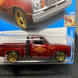 May include: A maroon Hot Wheels Dodge pickup truck toy in its original blister packaging. The truck features gold-colored wheels, a black exhaust stack, and gold text on the door that reads Will U Be My Valentine. The card shows a 3/10 label.