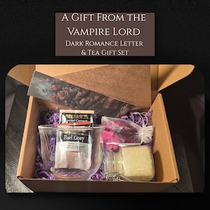 May include: A gift set in a cardboard box, including a clear glass mug with an Earl Grey tea bag, a Bigelow tea packet, a candle, and dried flowers. The box also contains a decorative card with roses and the text "A GIFT FROM THE VAMPIRE LORD DARK ROMANCE LETTER & TEA GIFT SET."