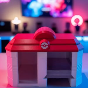 Pode incluir: Uma caixa de armazenamento vermelha e branca com um telhado vermelho e um emblema circular. A caixa tem dois compartimentos abertos e parece ser projetada para guardar cartas. O fundo está desfocado, com luzes coloridas.