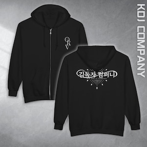 Puede incluir: Sudadera con capucha negra con cremallera y logotipo blanco en el pecho y la espalda. El logotipo frontal es un diseño estilizado "QRV". La parte trasera presenta texto coreano y las palabras "KIM DOK JA COMPANY" en blanco. La sudadera tiene capucha y bolsillo delantero.